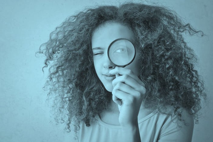 Eine junge Dame schaut durch eine Lupe – repräsentiert die sorgfältige Prüfung und die einzigartigen Spezialversicherungen von RIANEVA, die optimale Absicherung gewährleisten.