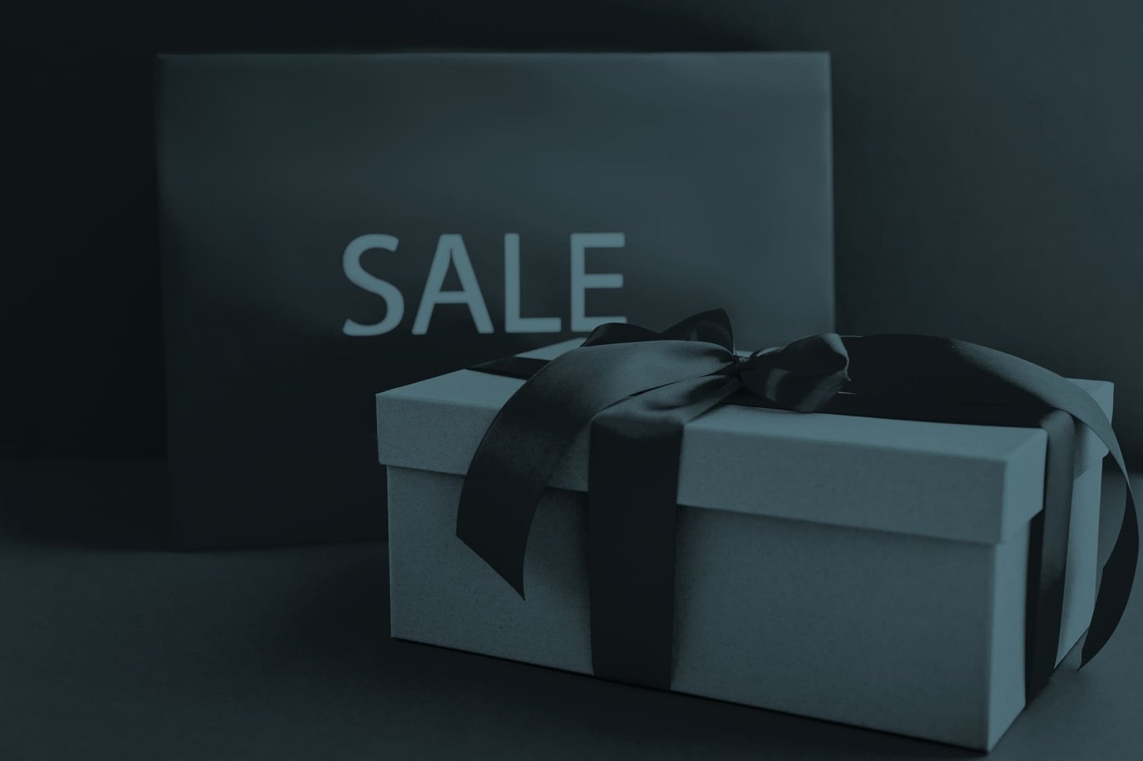 Geschenkbox mit Masche im Vordergrund und ein riesiges Kuvert mit der Aufschrift SALE im Hintergrund – alles im markanten RIANEVA-Design.